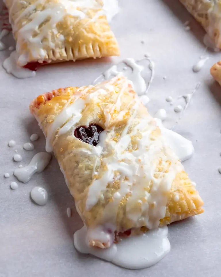 A rectangle puff pastry filled with cherry filling and a vanilla drizzle on top of it.