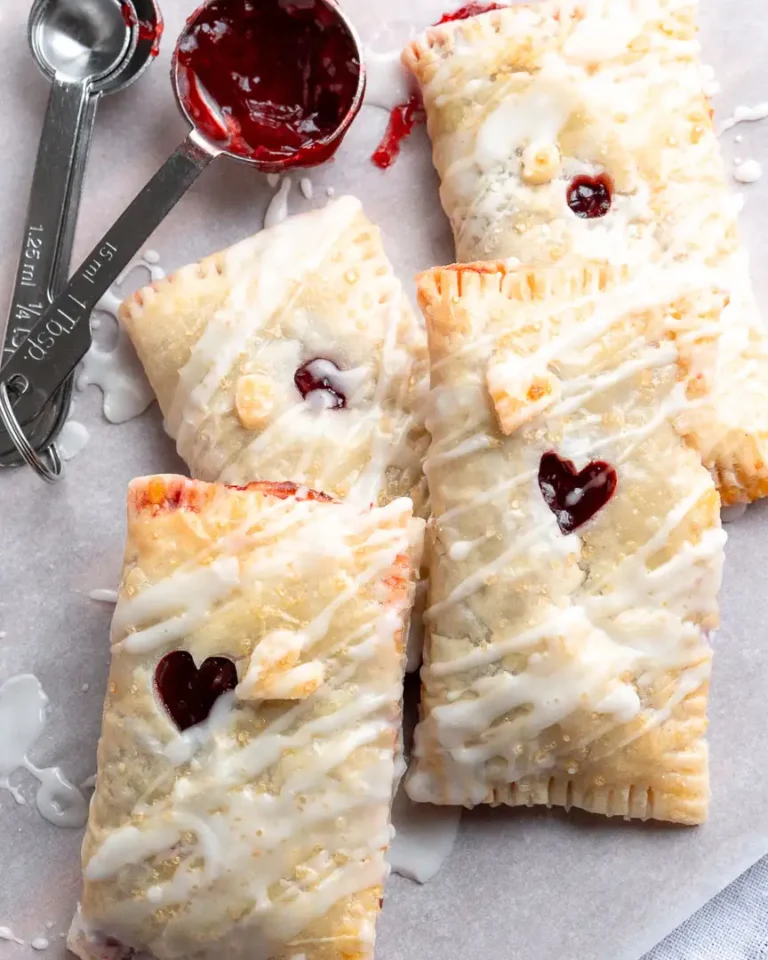 Rectangles of puff pastry filled with cherry filling piled on top of each other. They have a small hole in the middle to let the filling peak out and they have a drizzle of frosting on them.