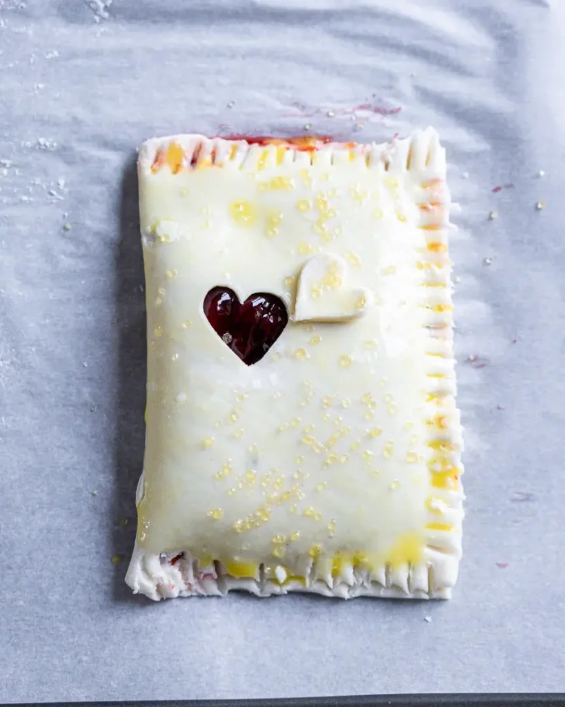 An unbaked cherry turnover brushed with an egg wash then sprinkled with raw turbinado sugar.