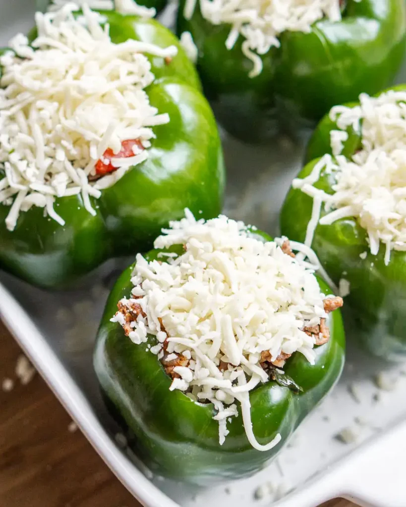 Stuffed bell peppers with shredded mozzarella cheese on top ready to be baked.