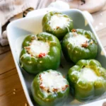 A baking pan of 5 stuffed peppers with melted mozzarella cheese on top of each pepper.