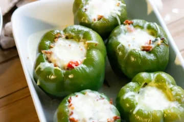 A baking pan of 5 stuffed peppers with melted mozzarella cheese on top of each pepper.