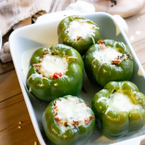 A baking pan of 5 stuffed peppers with melted mozzarella cheese on top of each pepper.