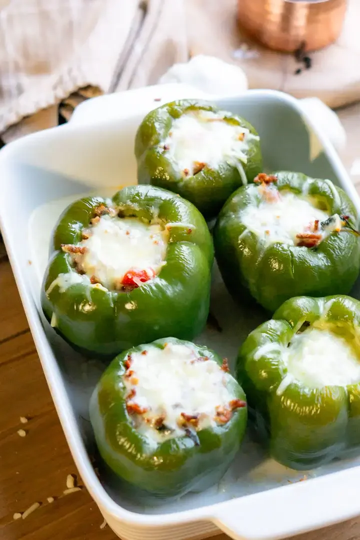 A baking pan of 5 stuffed peppers with melted mozzarella cheese on top of each pepper.