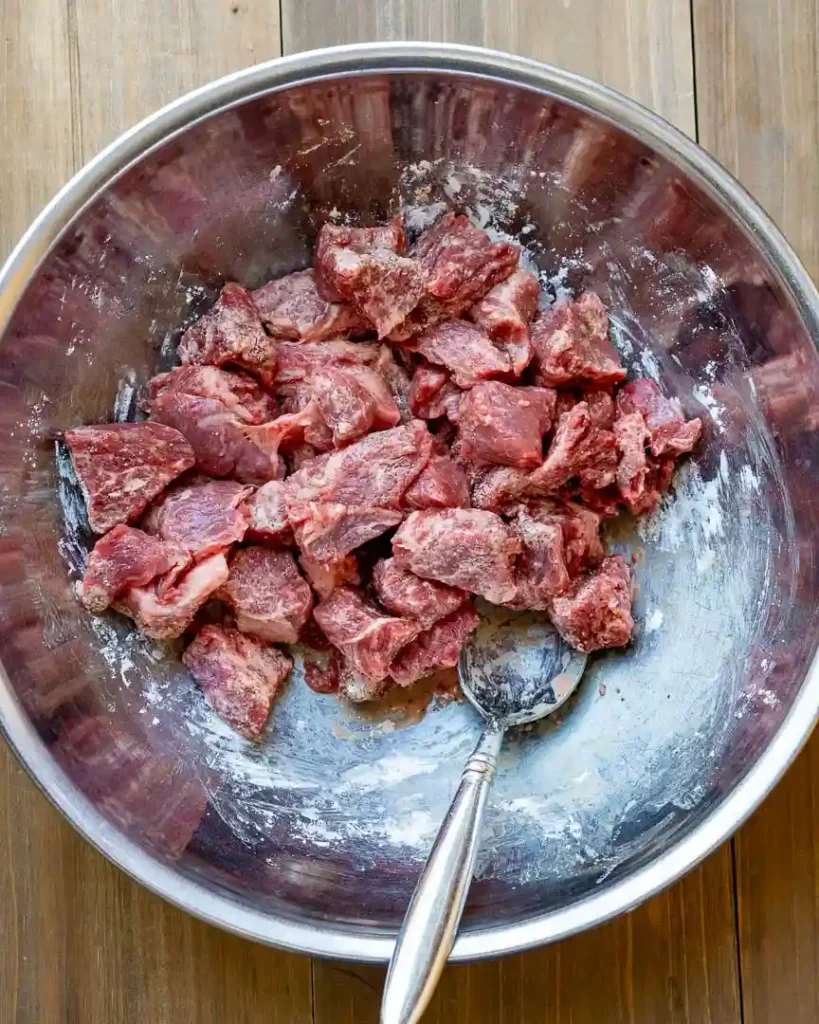 Raw beef cubes in a bowl coated with cornstarch.