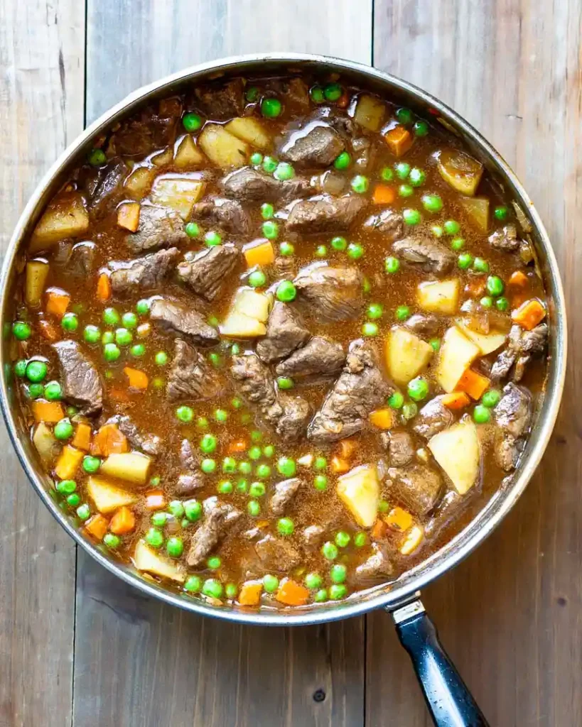 A skillet with beef, peas, carrots, potatoes in a gravy.