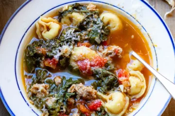 Tortellini and Sausage soup in a bowl with a spoon and grated cheese on top