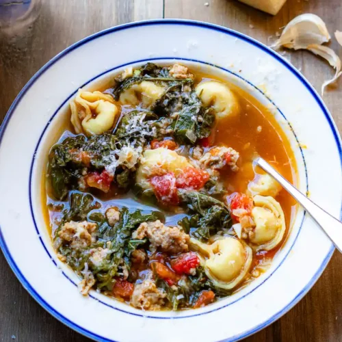 Tortellini and Sausage soup in a bowl with a spoon and grated cheese on top