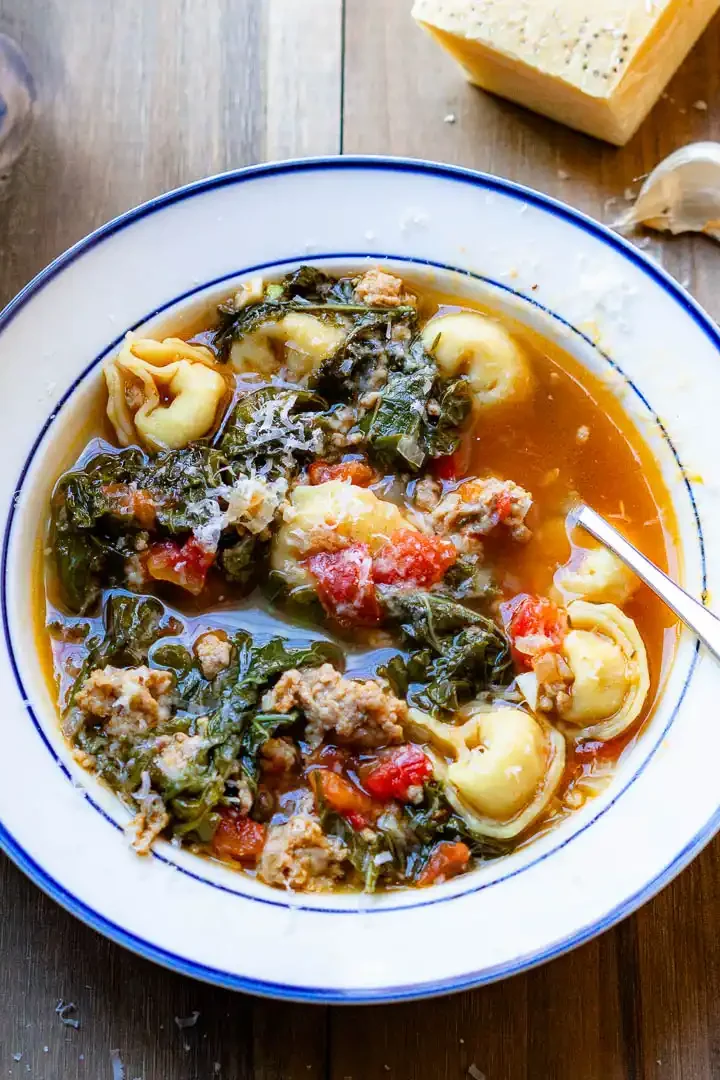 Tortellini and Sausage soup in a bowl with a spoon and grated cheese on top