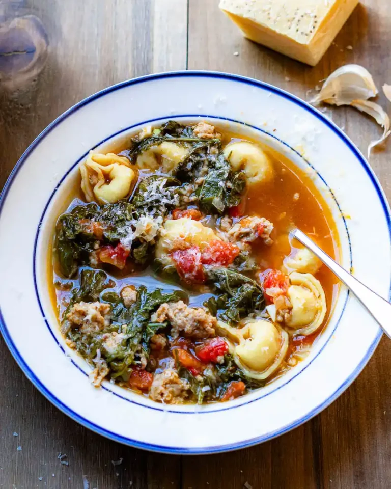 Tortellini and Sausage soup in a bowl with a spoon and grated cheese on top