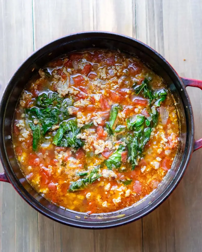 A pot of soup with tomatoes and greens.