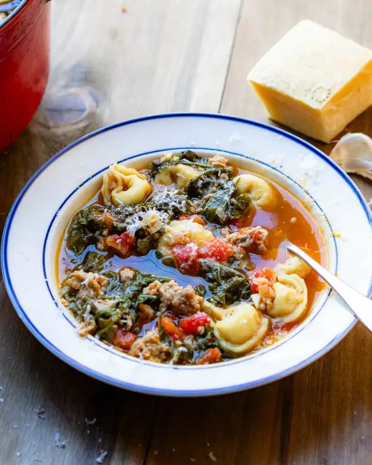 A bowl of tortellini soup with a spoon.